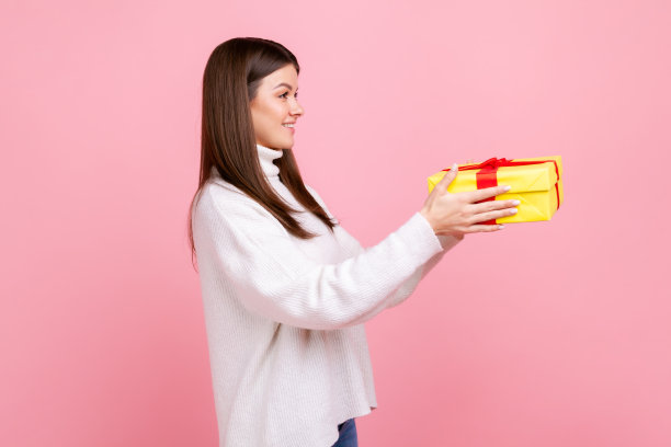 侧面的照片，年轻的黑发女性手持黄色包装的礼品盒，给予礼物图片下载