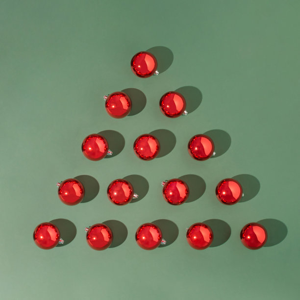 三角形由红色圣诞小玩意制成，在绿色背景上有阳光照射的阴影。最小的新年概念。图片下载