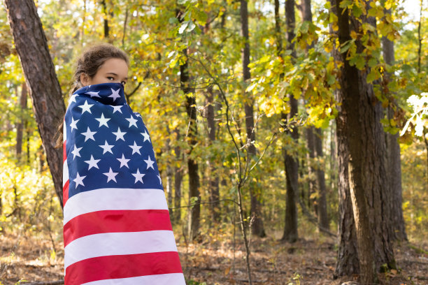 一个严肃的小女孩用一面美国国旗遮住了她的脸。图片下载