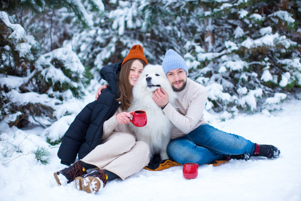 一对年轻的夫妇和一只漂亮的萨摩耶犬在雪地森林里喝茶，新年快乐，圣诞快乐图片下载
