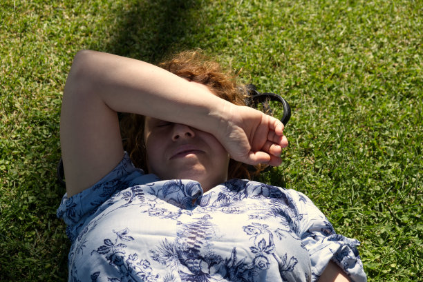 一个白人妇女在草地上睡着了，她用手臂蒙住脸，让阳光照进她的眼睛图片下载