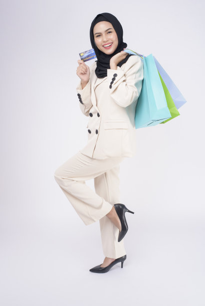 年轻美丽的穆斯林妇女在西装手持彩色购物袋在白色背景工作室图片下载