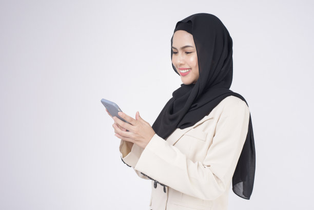 年轻美丽的穆斯林女人的肖像在白色的背景下使用智能手机图片下载