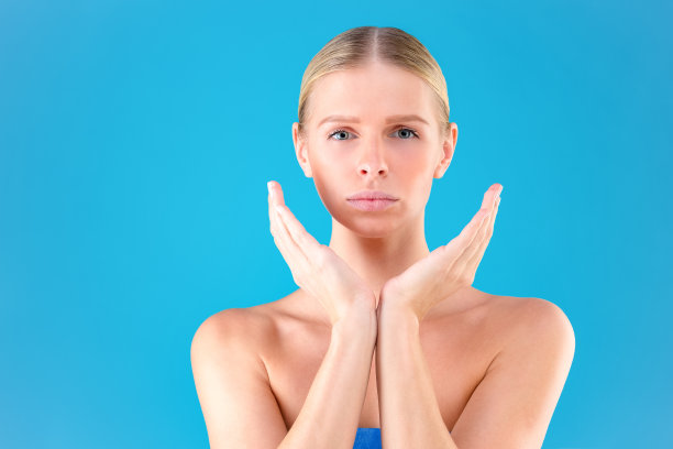 接近的肖像华丽的美丽和好看的年轻女人与无瑕的皮肤。她用手捂住孤立在蓝色背景上的脸颊图片下载