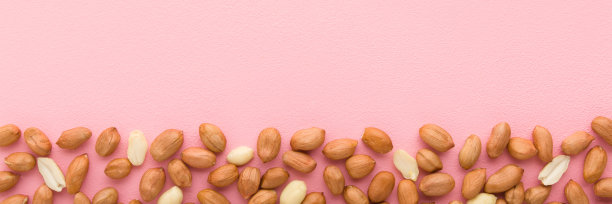 浅粉色桌子背景上的棕色杏仁坚果。柔和的颜色。特写镜头。食物宽横幅。为文本空出位置。自顶向下的观点。图片下载