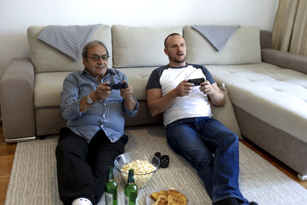 白种人的父亲和成年的儿子一起在客厅玩电子游戏。图片下载