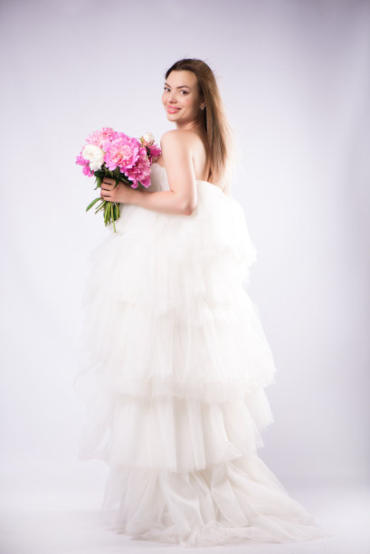 美丽开朗的年轻金发女孩穿着裙子，孤立地站在白色的背景下，手捧一束牡丹图片下载