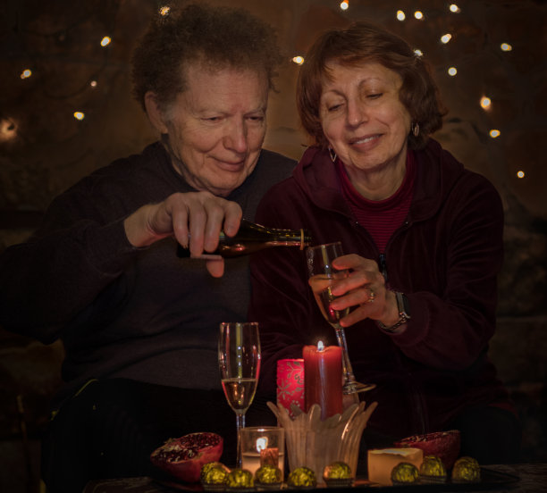 老夫妇坐在烛光和圣诞灯昏暗的房间里，用葡萄酒和巧克力庆祝图片下载