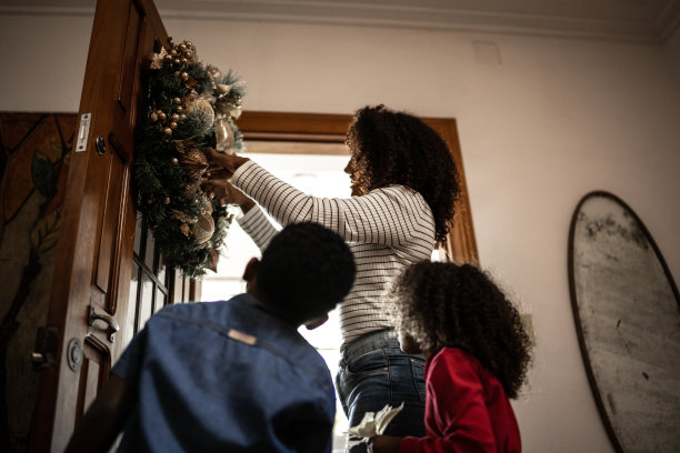母亲和孩子们在家里的门上挂一个圣诞花环图片下载