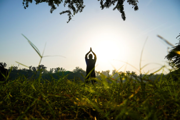 太阳和河流附近的公园里一个男孩做瑜伽的剪影-健康概念图片下载
