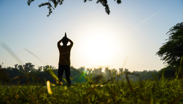 太阳和河流附近的公园里一个男孩做瑜伽的剪影-健康概念图片下载