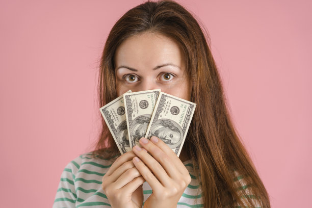 一个穿着休闲装的美丽的黑发女人在抽奖中赢得了一小笔钱。一个脸上盖着美钞的女孩的肖像图片下载