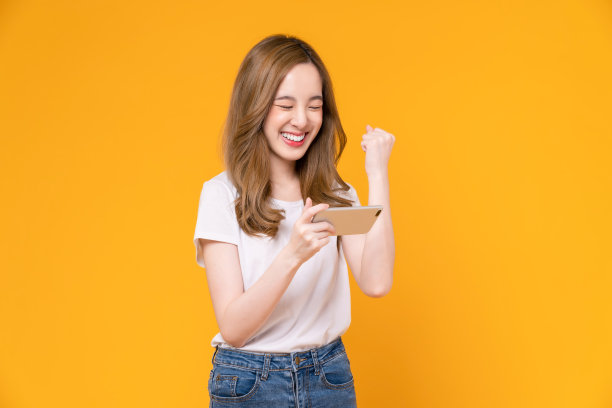 兴奋的年轻亚洲女人在橙色背景下用智能手机玩游戏。图片下载