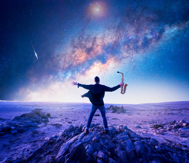 在智利的阿塔卡马沙漠，一个音乐家或萨克斯管吹奏者的剪影，在繁星点点的夜空下，在一块岩石上张开双臂图片下载