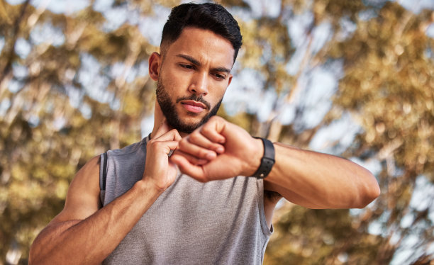 一个英俊的年轻人独自站在外面，在跑步后用手表测量脉搏图片下载