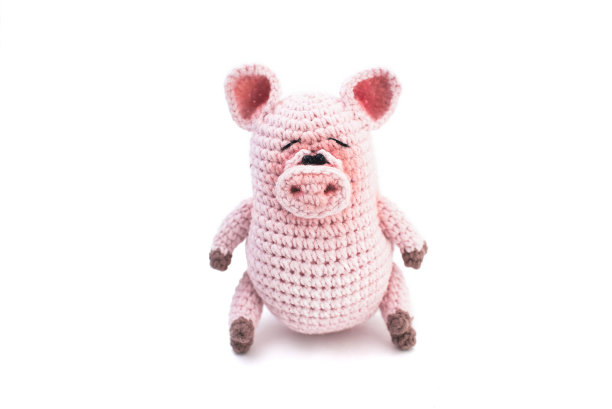 手工编织软玩具。Amigurumi。白色背景上的粉色小猪。钩针填充动物玩具。图片下载