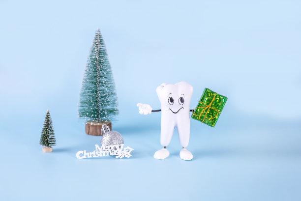 一个卡通牙齿模型，一个礼品盒，圣诞树，一个球和题词——蓝色背景上的圣诞快乐图片下载