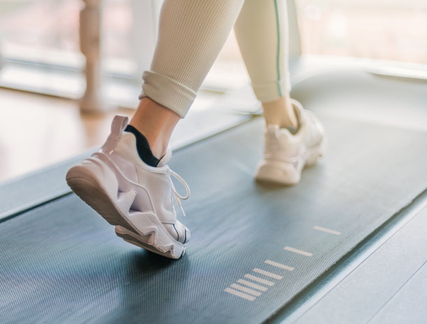 选择性模糊的腿跑在跑步机上。温暖的光线从背景的窗户进入。细节框框和特写。图片下载