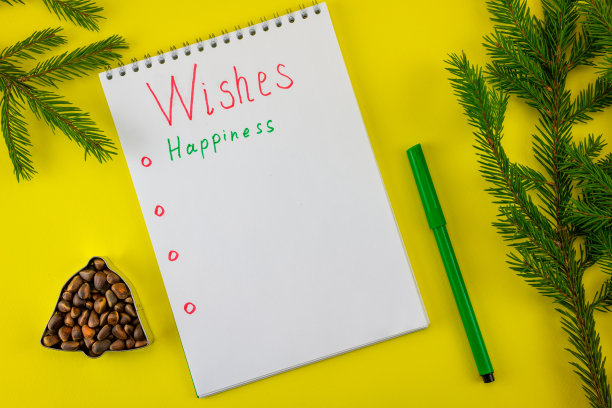 笔记本与圣诞老人的愿望在一个黄色的圣诞背景与钟云杉坚果。图片下载