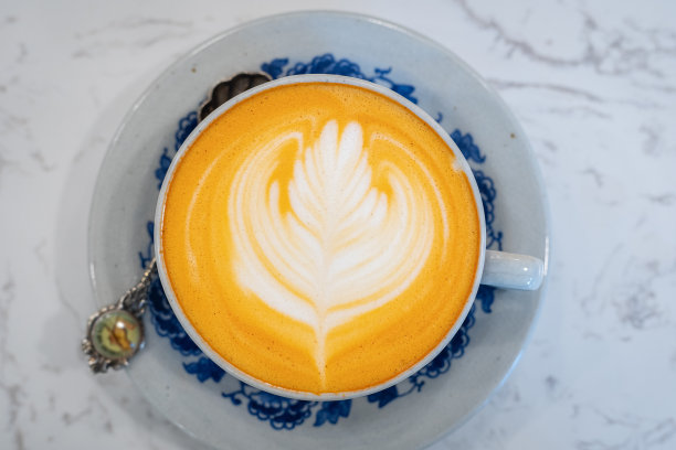 在一家咖啡店，热的泰国茶拿铁，拿铁艺术牛奶泡沫杯，大理石地板背景桌子。图片下载
