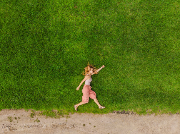 一名年轻女子躺在田野中央，用无人机拍了一张轻松的照片图片下载