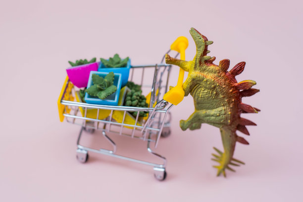 有趣的绿色恐龙玩具与购物车的花盆在一个软粉红色的背景图片下载