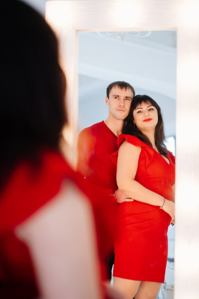 一个迷人的胖乎乎的女人穿着红色的裙子和一个男人看着镜子。图片下载