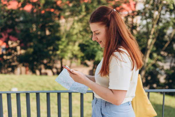 迷人的年轻女游客正在探索新的城市。快乐的红发女人与地图和智能手机在新的地方迷路，放松或旅行的概念图片下载