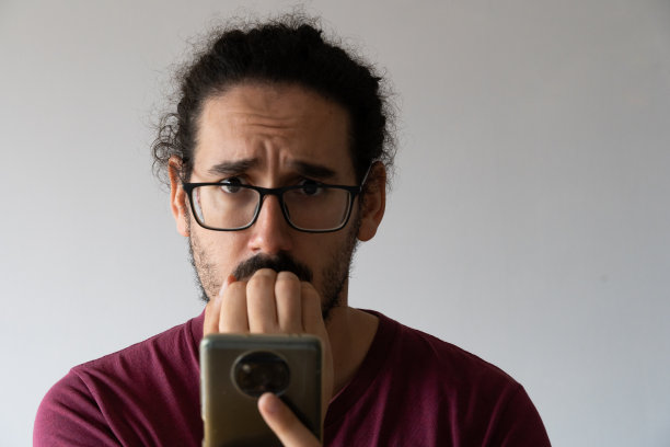一个焦虑的男人拿着智能手机咬指甲，看着镜头图片下载