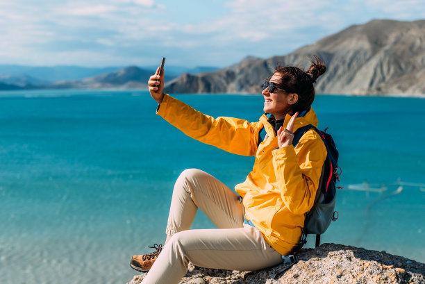 一名旅行者以大海为背景用手机自拍，特写镜头。在海滨的旅行者。一个女孩手里拿着手机，背景是美丽的大海。图片下载