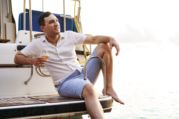 一个年轻人在游船的露天甲板上拿着一杯葡萄酒图片下载