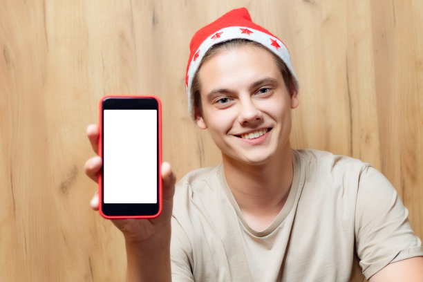 一名戴着圣诞老人帽子的男子正在使用手机。人手持智能手机进行视频通话和交流，应用概念与空白屏幕为模板和复制空间图片下载