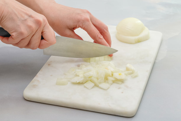 妇女双手在大理石砧板上切着白洋葱。一步一步的烹饪过程，静物，食谱图片下载