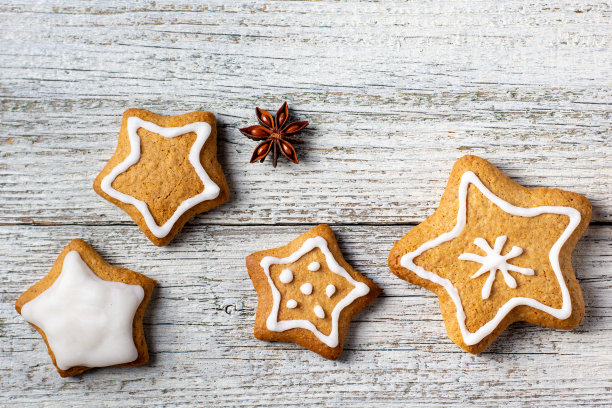 圣诞姜饼的边缘在一个星星的形状与釉色和香料的图案在白色木制背景。图片下载