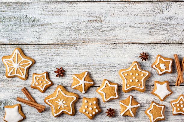 圣诞姜饼的边缘在一个星星的形状与釉色和香料的图案在白色木制背景。图片下载