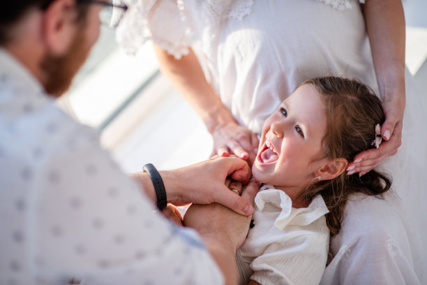 小女孩笑着躺在怀孕的妈妈的膝盖上，爸爸挠了挠女儿。幸福的家庭图片下载