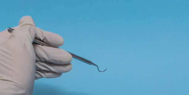 一套金属牙医的医疗设备工具，蓝色背景上的人工颌，人类的手握住工具，一套牙齿在水的杯子里。图片下载