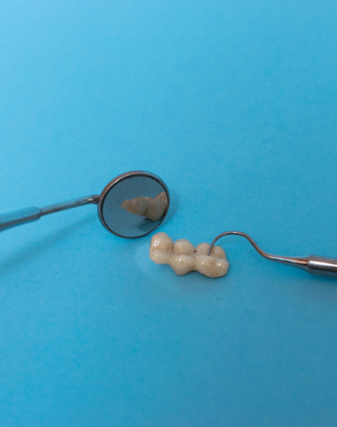 一套金属牙医的医疗设备工具，蓝色背景上的人工颌，人类的手握住工具，一套牙齿在水的杯子里。图片下载