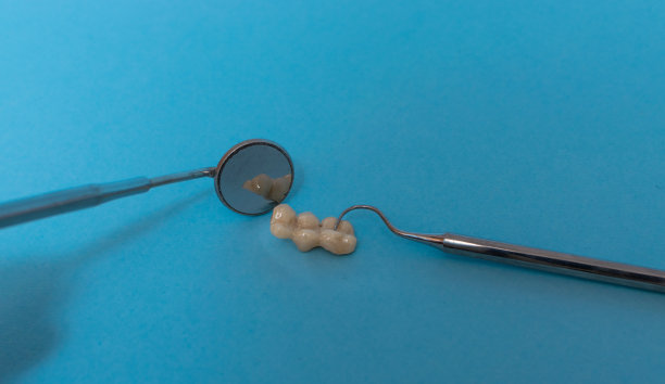 一套金属牙医的医疗设备工具，蓝色背景上的人工颌，人类的手握住工具，一套牙齿在水的杯子里。图片下载