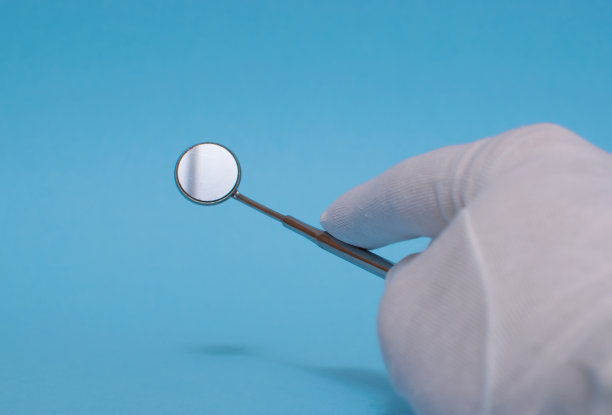 一套金属牙医的医疗设备工具，蓝色背景上的人工颌，人类的手握住工具，一套牙齿在水的杯子里。图片下载