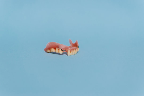 一套金属牙医的医疗设备工具，蓝色背景上的人工颌，人类的手握住工具，一套牙齿在水的杯子里。图片下载