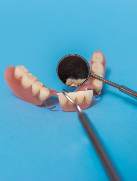 一套金属牙医的医疗设备工具，蓝色背景上的人工颌，人类的手握住工具，一套牙齿在水的杯子里。图片下载