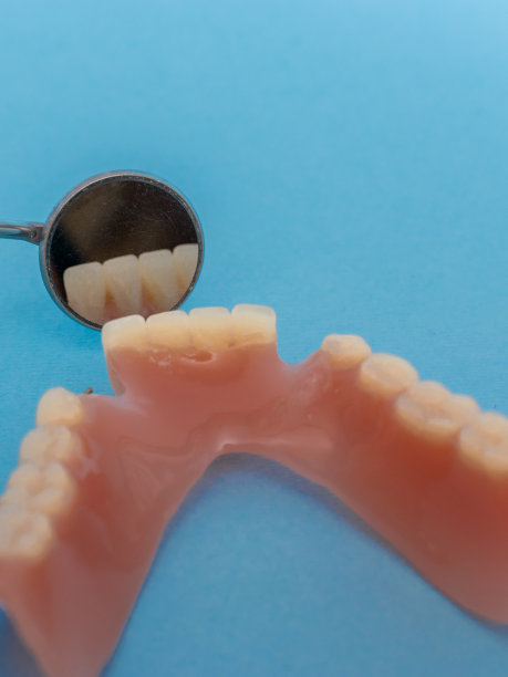 一套金属牙医的医疗设备工具，蓝色背景上的人工颌，人类的手握住工具，一套牙齿在水的杯子里。图片下载