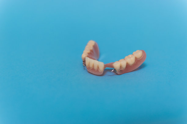 一套金属牙医的医疗设备工具，蓝色背景上的人工颌，人类的手握住工具，一套牙齿在水的杯子里。图片下载