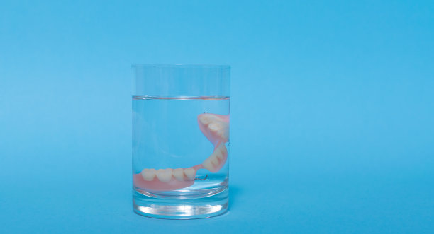 一套金属牙医的医疗设备工具，蓝色背景上的人工颌，人类的手握住工具，一套牙齿在水的杯子里。图片下载