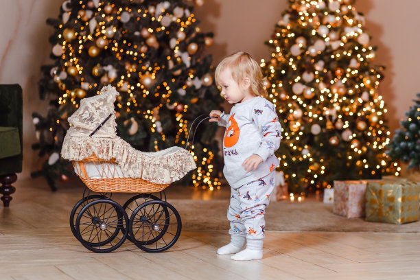 穿着睡衣微笑的小女孩在圣诞屋玩玩具婴儿车。孩子们在圣诞节等待礼物图片下载