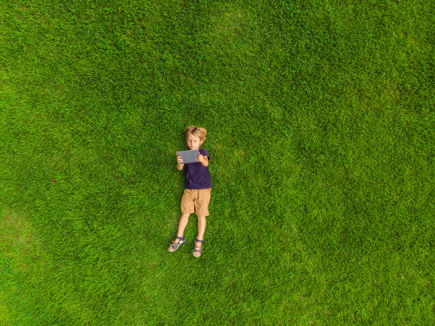 男孩躺在公园的草地上，看着石碑。无人机和四旋翼飞机的照片图片下载