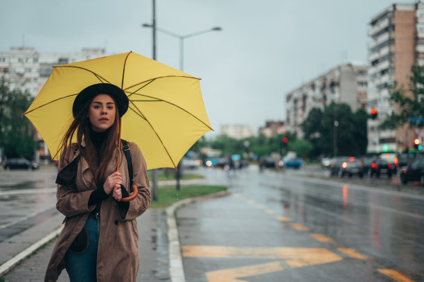 年轻漂亮的女人拿着黄色雨伞，用着智能手机图片下载
