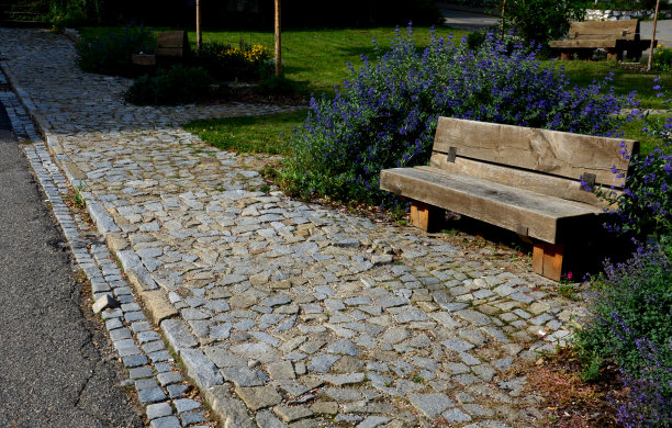 公园休息的地方，用实木制成的长凳连接到木屋的木钉上。这些长凳背靠背连在一起。草坪和开花的观赏灌木。图片下载