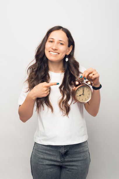 一名年轻女子指着闹钟的垂直照片。图片下载